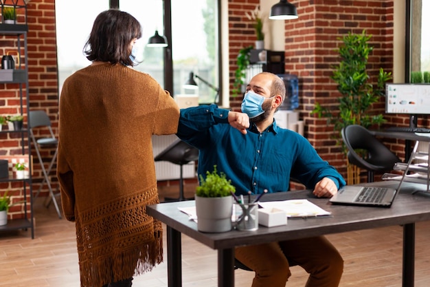 Équipe d'affaires avec masque de protection médicale pour prévenir l'infection par le coronavirus touchant le coude tout en travaillant dans le bureau de démarrage. Homme d'affaires analysant la stratégie de l'entreprise de saisie de graphique de données