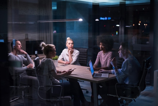 Équipe d'affaires multiethnique en démarrage lors d'une réunion dans un brainstorming intérieur de bureau de nuit moderne, travaillant sur un ordinateur portable
