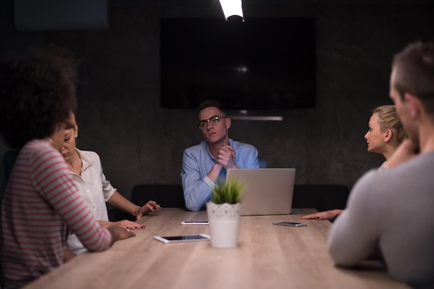 Équipe d'affaires multiethnique en démarrage lors d'une réunion dans un brainstorming intérieur de bureau de nuit moderne, travaillant sur un ordinateur portable
