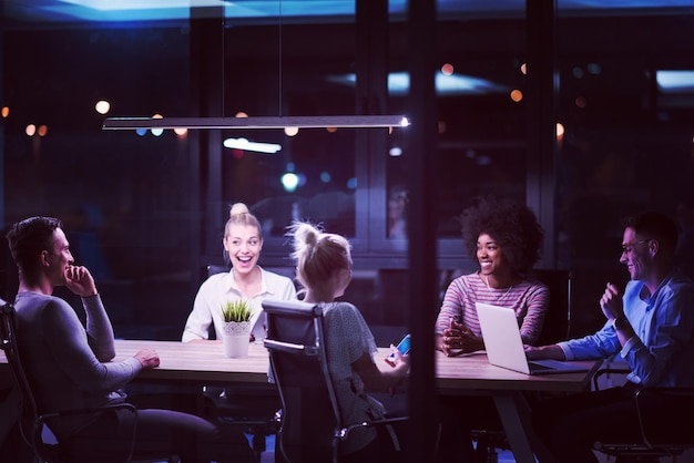 Équipe d'affaires multiethnique en démarrage lors d'une réunion dans un brainstorming intérieur de bureau de nuit moderne, travaillant sur un ordinateur portable