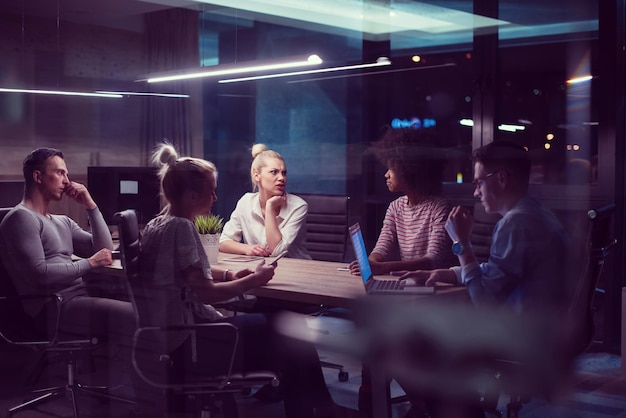 Équipe d'affaires multiethnique en démarrage lors d'une réunion dans un brainstorming intérieur de bureau de nuit moderne, travaillant sur un ordinateur portable