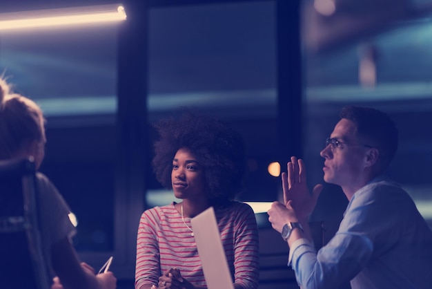 Équipe d'affaires multiethnique en démarrage lors d'une réunion dans un brainstorming intérieur de bureau de nuit moderne, travaillant sur un ordinateur portable