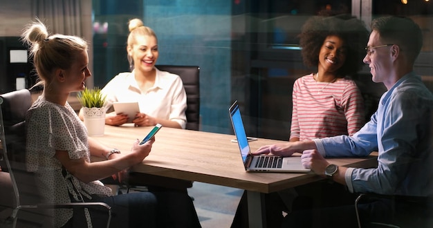 Équipe d'affaires multiethnique en démarrage lors d'une réunion dans un brainstorming intérieur de bureau de nuit moderne, travaillant sur un ordinateur portable