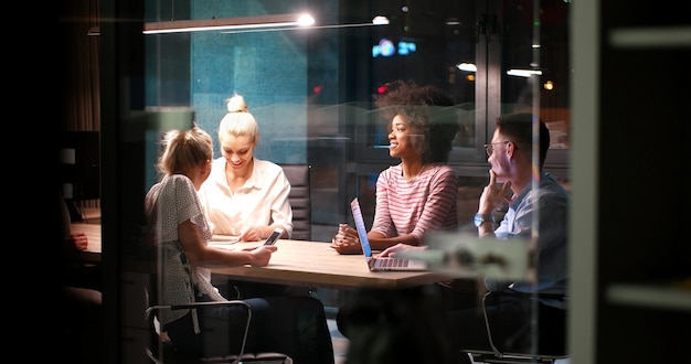 Équipe d'affaires multiethnique en démarrage lors d'une réunion dans un brainstorming intérieur de bureau de nuit moderne, travaillant sur un ordinateur portable