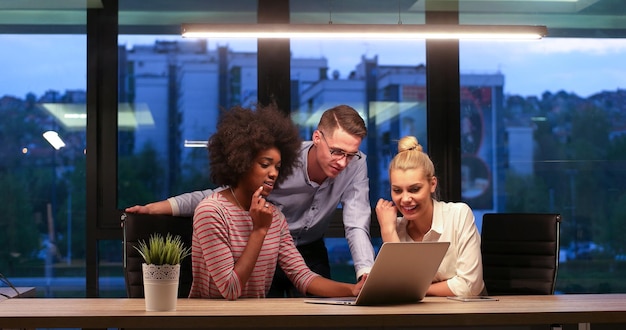 Équipe d'affaires multiethnique en démarrage lors d'une réunion dans un brainstorming intérieur de bureau de nuit moderne, travaillant sur un ordinateur portable