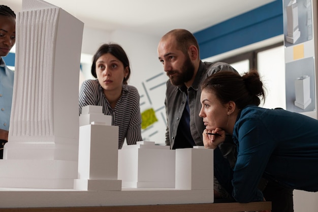 Équipe d'architectes professionnels regardant la maquette du gratte-ciel dans le bureau d'architecture. Partenaires ingénieurs travaillant sur un projet de groupe au bureau avec un modèle de construction immobilière.