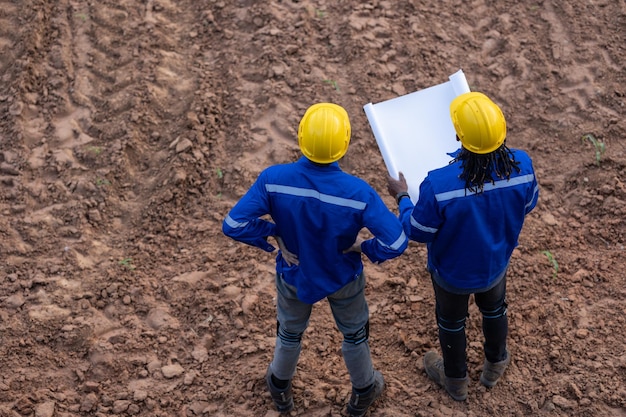 Équipe d'arpenteurs travaillant ensemble sur le terrain de construction consulter l'étude de l'emplacement du bâtiment avec le plan d'étage