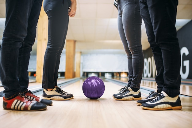 Équipe de bowling, pieds des joueurs en chaussures de maison et balle sur voie. Amis jouant au jeu en club, loisirs actifs