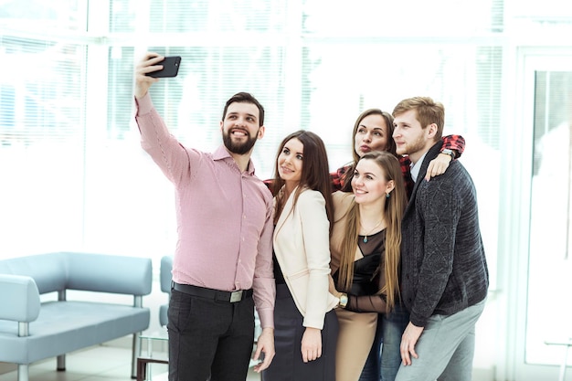 Équipe commerciale amicale prenant un selfie en se tenant près de la fenêtre du bureau