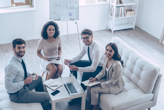 Équipe commerciale créative. Vue de dessus du groupe de quatre jeunes regardant la caméra avec le sourire alors qu'il était assis sur le canapé au bureau