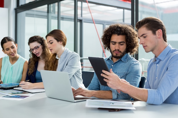 Équipe commerciale discutant sur ordinateur portable et tablette numérique en réunion