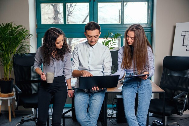 Équipe commerciale de jeunes architectes ou designers créant un nouveau projet tout en travaillant dans le bureau moderne et élégant avec grande fenêtre.