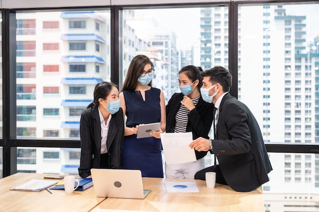 Équipe commerciale multiethnique portant un masque facial lors d'une réunion d'affaires dans un nouveau bureau normal Divers collègues d'entreprise faisant un brainstorming avec un appareil technologique et des documents commerciaux