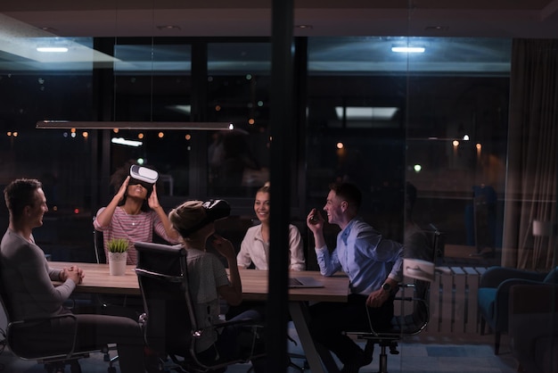 Équipe commerciale multiethnique utilisant un casque de réalité virtuelle lors d'une réunion de bureau de nuit Les développeurs se réunissent avec un simulateur de réalité virtuelle autour d'une table dans un bureau créatif.