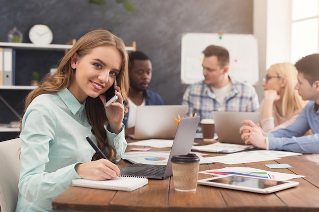 Équipe commerciale parlant des résultats de leur travail. Groupe d'hommes d'affaires joyeux discutant d'une nouvelle stratégie marketing, jeune femme parlant au téléphone et prenant des notes, espace de copie