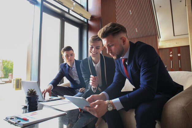 Équipe de démarrage d'entreprise lors d'une réunion dans un brainstorming intérieur de bureau moderne et lumineux, travaillant sur un ordinateur portable et une tablette.