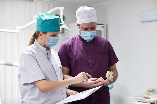 Équipe de dentistes se consultant au sujet du traitement dentaire tenant un modèle d'os de la mâchoire humaine