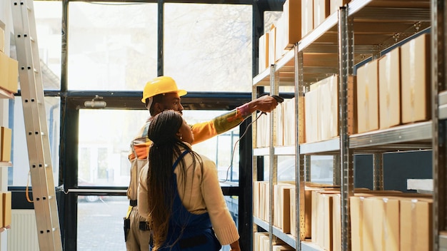 Équipe d'employés d'entrepôt travaillant sur l'inventaire, scannant les codes-barres sur les marchandises avec scanner et tablette. Homme et femme dans la salle de stockage vérifiant les produits et les fournitures, les packs d'expédition. Prise de vue au trépied.