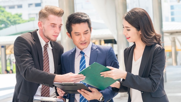 Équipe de gens d'affaires intelligent homme et femme parlent aux heures de pointe avec le dossier papier présent au piéton en plein air.