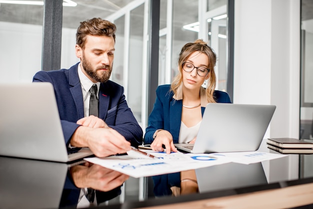 Équipe de gestionnaires analytiques travaillant avec des graphiques papier et des ordinateurs portables au bureau