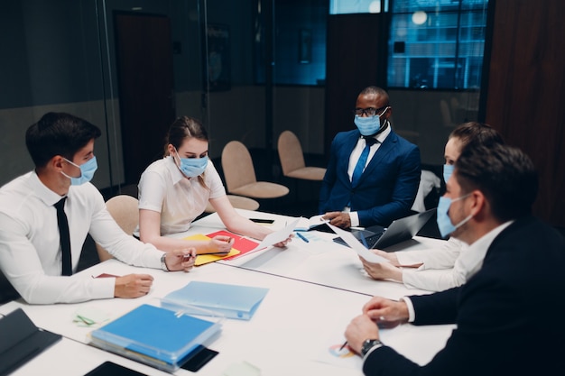 Équipe d'hommes d'affaires et de femmes d'affaires portant un masque médical lors d'une réunion de bureau. Discussion de conférence de groupe de gens d'affaires avec le patron.