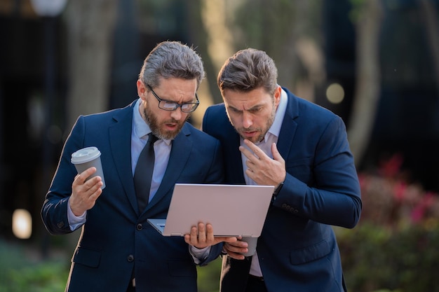 Équipe d'hommes d'affaires utilisant un ordinateur portable hommes d'affaires en plein air à la recherche d'ordinateur portable avec leur succès commercial dans la ville