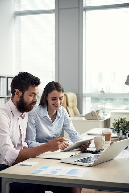 Équipe de jeunes managers caucasiens assis à une table de bureau et utilisant une tablette tout en travaillant sur un nouveau projet