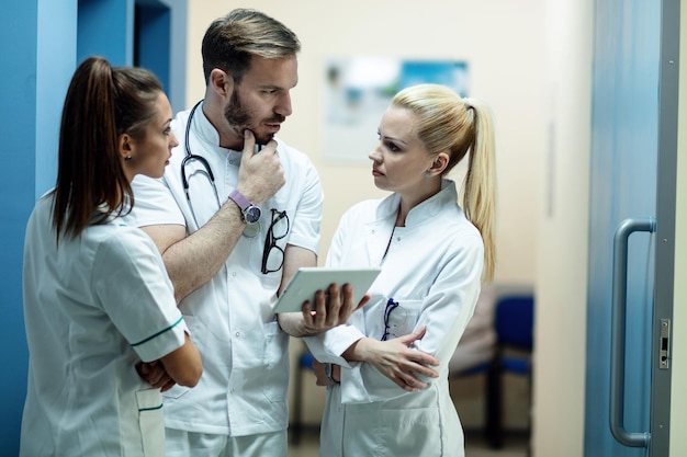 Équipe de médecins discutant des rapports médicaux des patients tout en utilisant une tablette numérique dans un couloir de l'hôpital