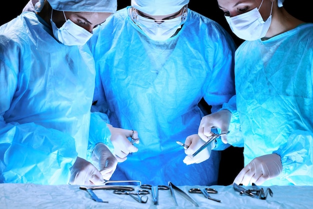 Équipe médicale effectuant une opération. Groupe de chirurgiens au travail en salle d'opération en bleu.