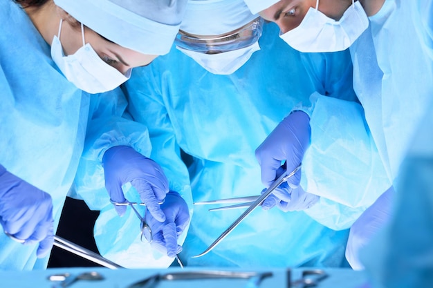 Équipe médicale effectuant une opération. Groupe de chirurgiens au travail en salle d'opération en bleu.