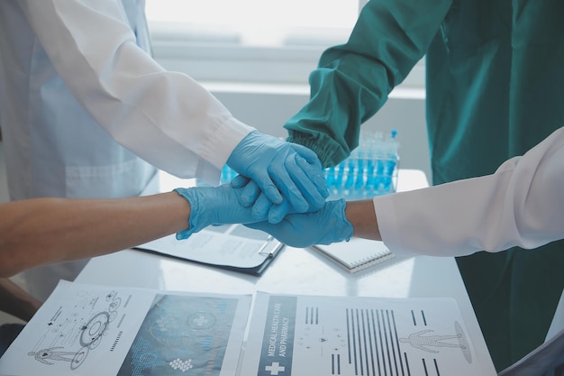 Équipe médicale multiraciale ayant une réunion avec des médecins en blouse blanche et en blouse chirurgicale assis à une table discutant des dossiers d'un patient