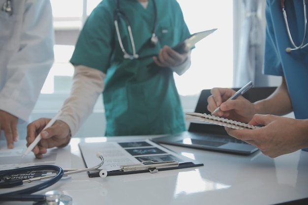 Équipe multiraciale de médecins discutant d'un patient debout regroupé dans le foyer regardant une tablette en vue rapprochée