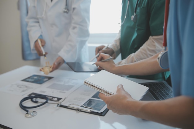 Équipe multiraciale de médecins discutant d'un patient debout regroupé dans le foyer regardant une tablette en vue rapprochée