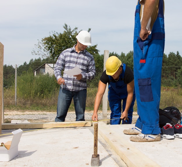 Équipe d'ouvriers sur un chantier de construction d'une maison neuve mesurant les poutres de support pour l'isolation des murs