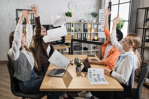 Équipe de partenaires féminins heureux et divers assis au bureau et vomissant des documents