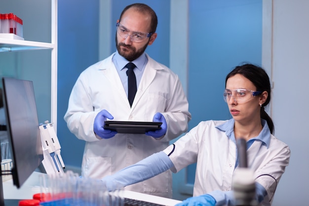 Équipe professionnelle de chercheurs en médecine travaillant ensemble dans un laboratoire stérile portant des lunettes de protection et une blouse blanche