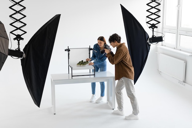 Équipe professionnelle de photographes et de gestionnaires de contenu tirant des chaussures élégantes dans un studio photo travaillant ensemble