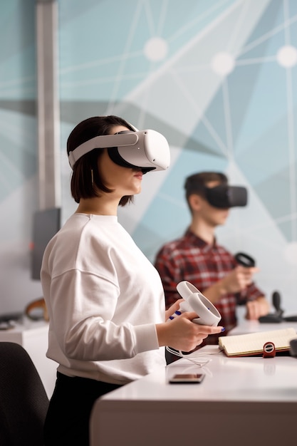 Équipe de quatre ingénieurs créatifs travaillant avec la réalité virtuelle, jeune femme testant des lunettes ou des lunettes VR assis dans la salle de bureau