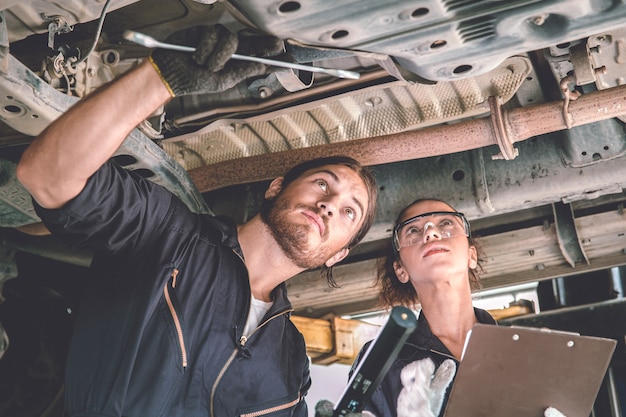 Équipe de travail de mécanicien automobile homme et femme contrôle sous la voiture pour l'entretien et le service automobile dans le garage