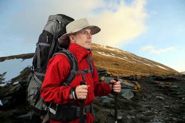 Équipé d'un voyageur dans une veste rouge avec des bâtons de randonnée regarde au loin