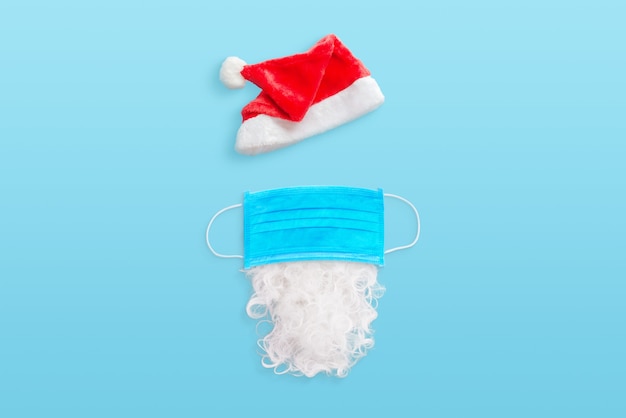 Équipement du père Noël dans le concept d'épidémie de coronavirus. Chapeau, masque et barbe sur le bureau bleu