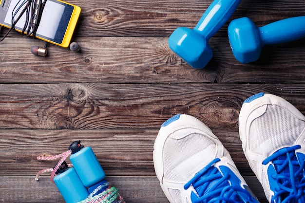 Équipement sportif - baskets, corde à sauter, haltères, smartphone et casque. Fond de sport sur plancher en bois, vue de dessus.