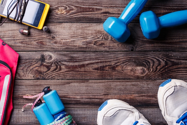 Équipement sportif - baskets, corde à sauter, haltères, smartphone et casque. Fond de sport sur plancher en bois, vue de dessus.