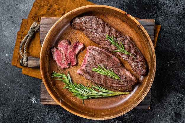 Rabat de surlonge frit ou bifteck de flanc de boeuf aux herbes dans une assiette en bois Fond noir Vue de dessus