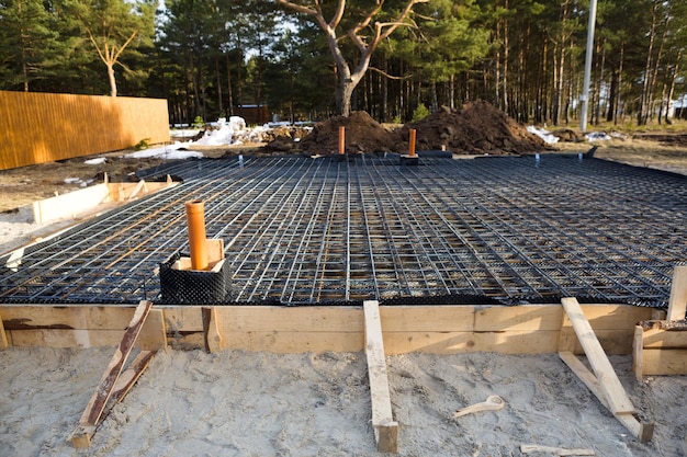 Les raccords en fer sur un coffrage en bois avec des tuyaux posés sont à la base du coulage des fondations de la maison avec une dalle de béton. Construction de chalets, conception, communication d'ingénierie.