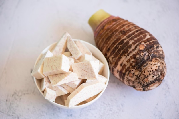 Racine de taro avec tranches de cubes sur fond de bol et de table, racine de taro biologique crue fraîche prête à cuire