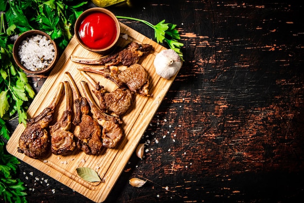 Rack d'agneau grillé sur une planche à couper avec du persil et de la sauce tomate