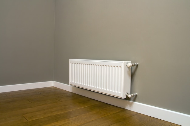 Radiateur de chauffage en métal blanc monté sur un mur gris à l'intérieur d'une pièce.