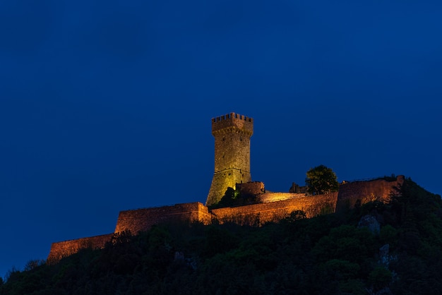 Radicofani, un village médiéval et forteresse en Toscane, Italie. Vue unique au crépuscule, la tour de pierre perchée sur une falaise rocheuse illuminée au crépuscule contre le ciel bleu.