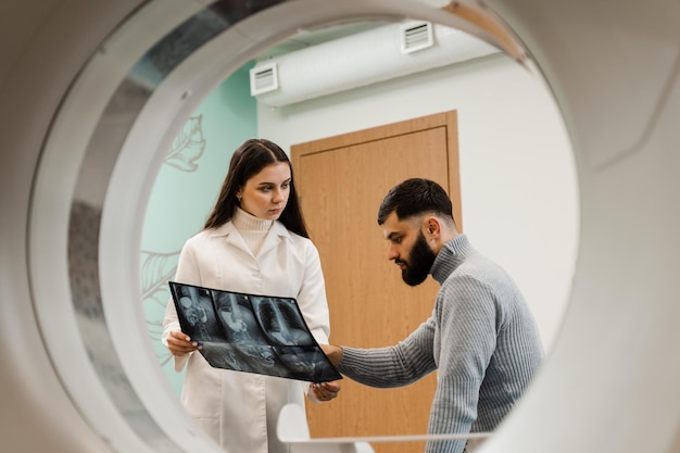 Radiologue en tomodensitométrie montrant une radiographie de l'abdomen à un patient homme dans une salle de tomodensitométrie Un médecin consultant un patient et montrant une radiographie pulmonaire à un patient dans une salle de tomodensitométrie